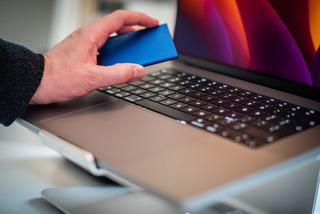Nahaufnahme einer Hand, die eine externe Festplatte über einer Laptop-Tastatur hält.
