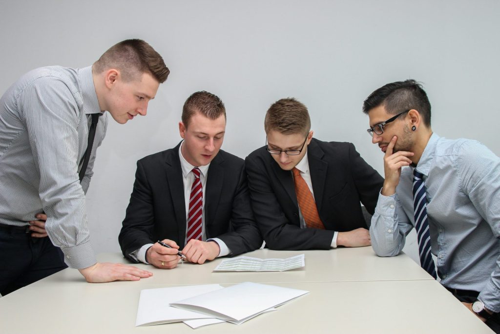 Vier Männer blicken auf das Papier auf dem Tisch.